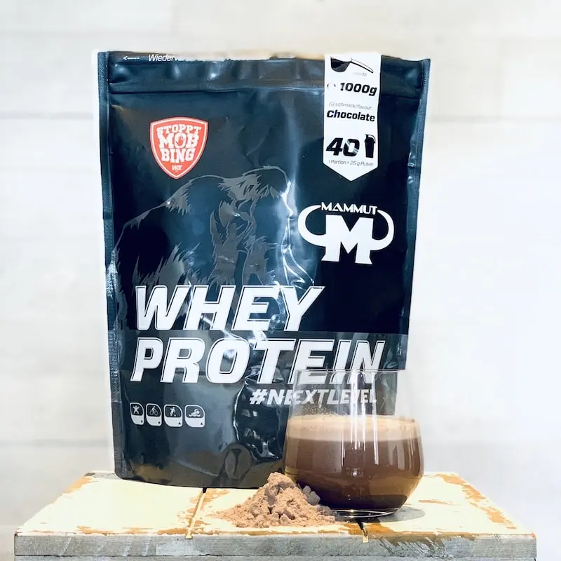 Unser Mammut-Whey-Schokolade-Beutel neben Pulver und angemischtem Schokoshake