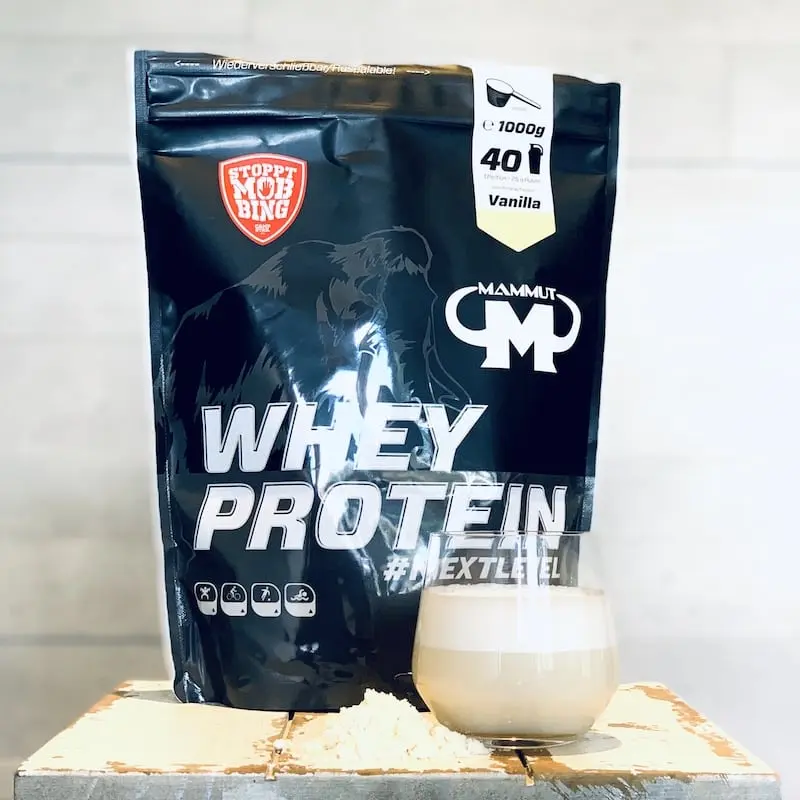 Unser Mammut-Whey-Vanille-Beutel neben Pulver und angemischtem Vanilleshake